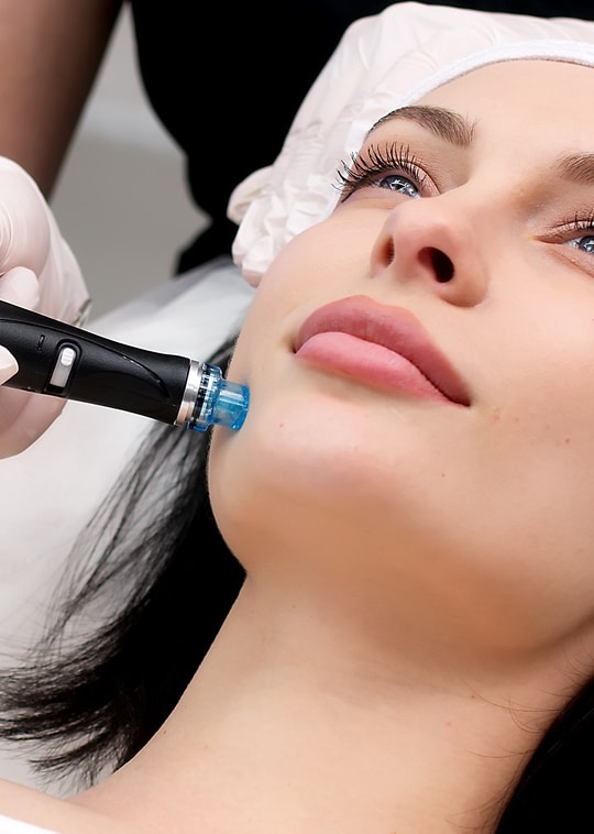 Cosmetology clinic. Professional female cosmetologist doing Hydradermabrasian procedure while being a work. Attractive nice woman lying on the medical bed while having beauty procedures